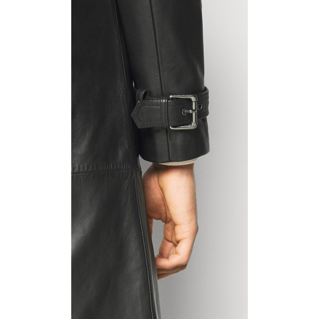 Close-up of model’s hand holding waist belt of men's black genuine leather trench coat, showing texture and stitching detail