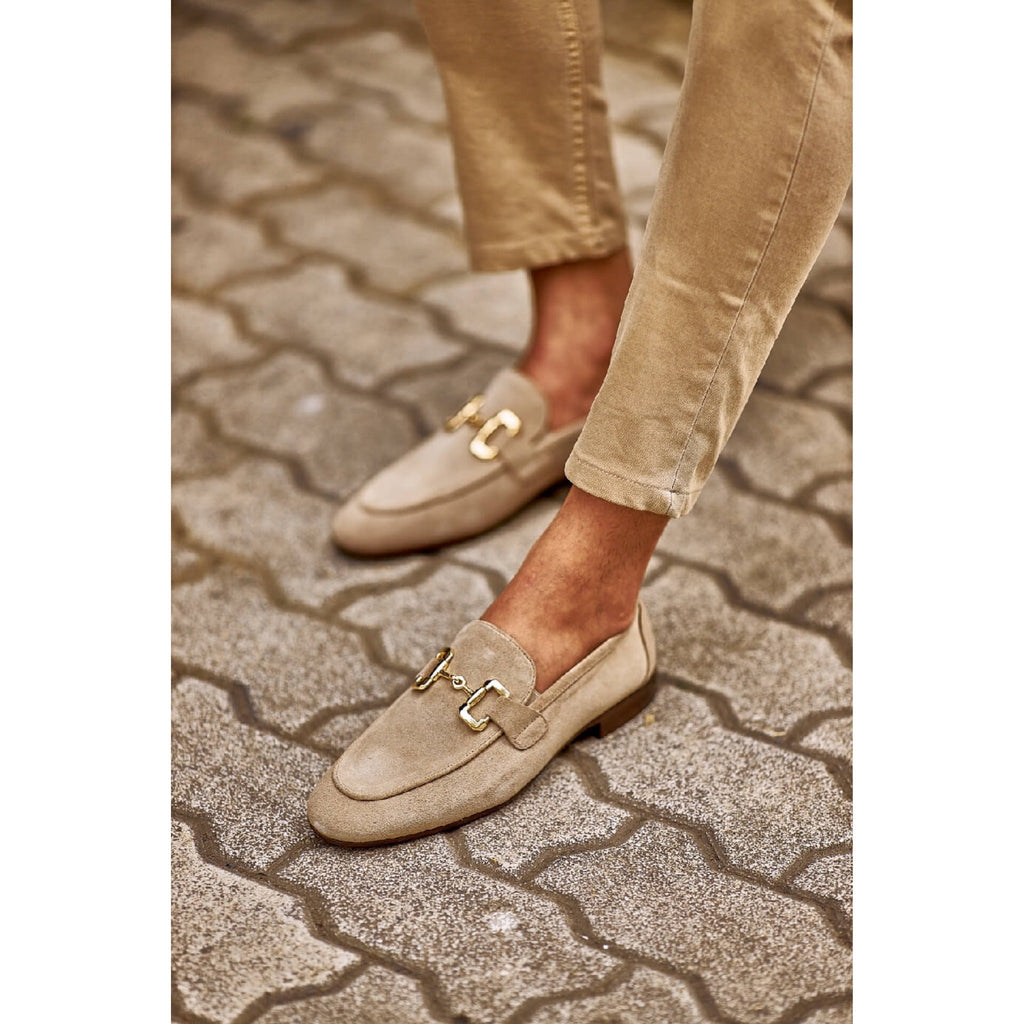 Men’s suede loafers in light beige with metal bit detailing – luxury slip-on shoes paired with rolled khaki trousers.