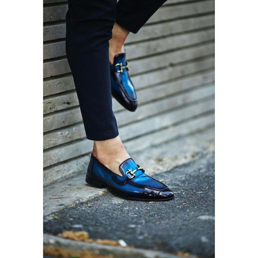 Premium blue leather loafers with a bold finish, worn with fitted black trousers – contemporary men’s fashion statement shoes.