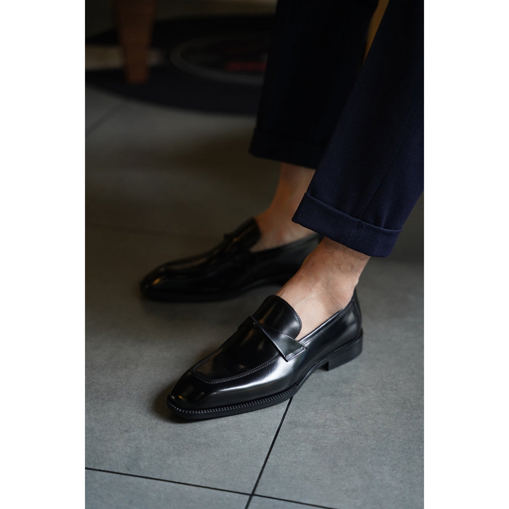 Black penny loafers paired with tailored navy trousers – timeless men’s leather shoes designed for versatile styling.