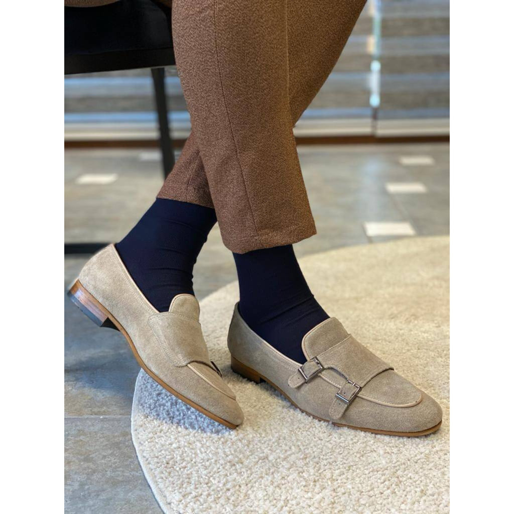 Front View of a man wearing beige suede double monk strap loafers with navy socks and brown textured trousers, standing near a marble step.